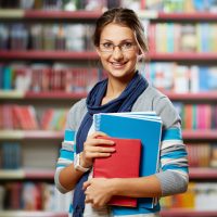 Portrait of clever student with books in college library